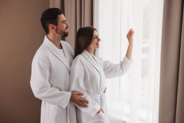 Otel odasının penceresinin yanında bornoz giyen mutlu çift.