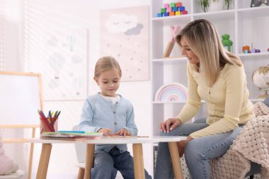 Anne, kızına beyaz masada alfabe öğretiyor.
