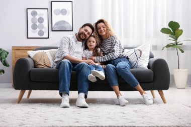 Mutlu ebeveynler evdeki kanepede kızlarına sarılıyorlar. Aile bağı