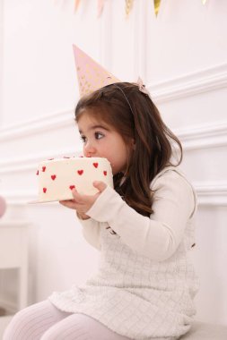 Doğum günü kutlaması. Parti şapkalı şirin küçük kız içeride lezzetli pastalar yiyor.