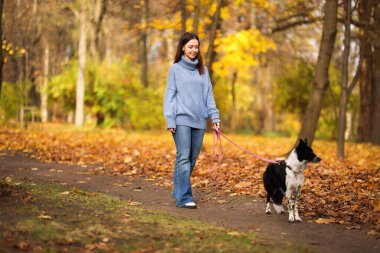 Sonbahar parkında sevimli köpeğini gezdiren bir kadın.