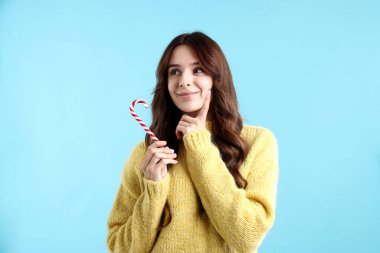 Açık mavi arka planda şeker kamışlı, düşünceli bir kadın. Mutlu Noeller ve mutlu yıllar.