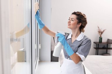 Oda hizmetçisi pencereyi paçavra ve deterjanla temizliyor.
