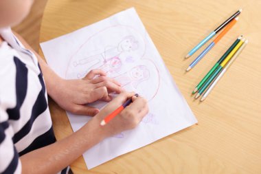 Ahşap masada aile çizen şirin küçük çocuk, yakın plan.