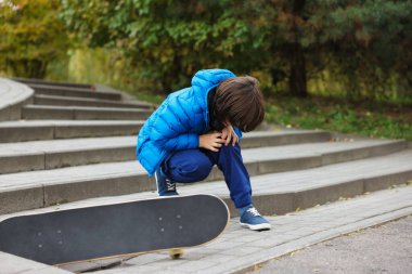 Dışarıda kaykay yaparken merdivenlerde diz ağrısı çeken küçük bir çocuk. Çocuk tehlikede.