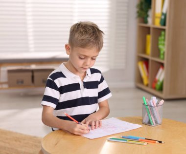 İçerideki ahşap masada resim çizen sevimli küçük çocuk.