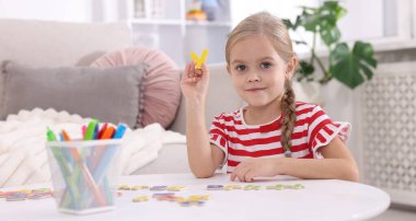 Beyaz masada harflerle alfabe öğrenen küçük bir kız.