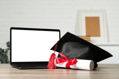 Diploma, mezuniyet şapkası ve dizüstü bilgisayar kapalı masa, yakın plan.