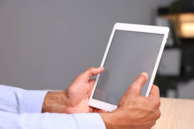 Kapalı alanda, ahşap masada tablet kullanan Afro-Amerikalı bir adam.
