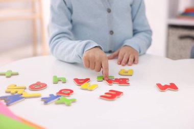 Beyaz masada harflerle alfabeyi öğrenen küçük kız, yakın plan.