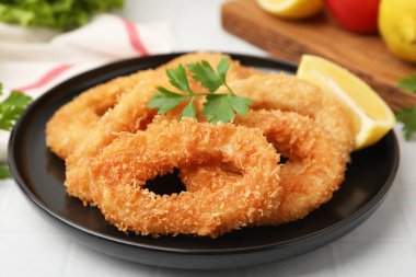 Kızarmış kalamar halkaları maydanozlu ve limon dilimli beyaz fayanslı masa, yakın plan.