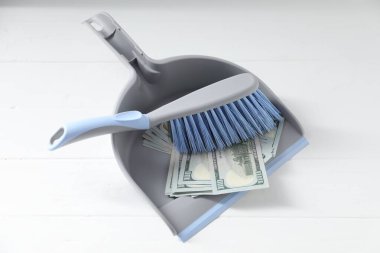 Beyaz ahşap yüzey üzerinde süpürge ve dolar banknotları olan faraş.