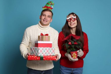 Noel aksesuarları, saksısı ve açık mavi arka planda hediyeleri olan mutlu çift.