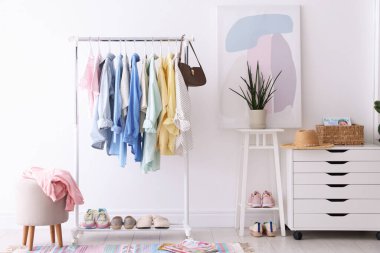 Beyaz duvarın yanında askıda asılı farklı şık kıyafetler, çanta ve ayakkabılar.