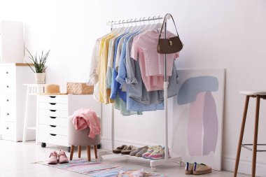 Askıda asılı farklı şık kıyafetler, aksesuarlar ve beyaz duvarın yanındaki ayakkabılar.