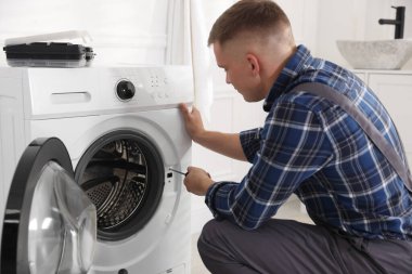 Üniformalı tamirci evde tornavidayla bozuk çamaşır makinesini tamir ediyor.