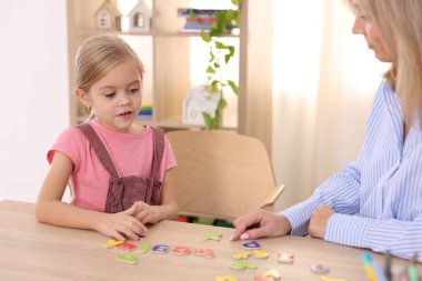 Konuşma terapisti kız alfabesini öğretiyor. Kapalı alanda, ahşap masada harflerle, yakın plan.