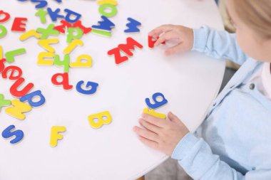 Beyaz masada harflerle alfabeyi öğrenen küçük kız, yakın plan.