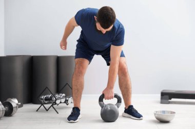 Spor salonunda kettlebell ile egzersiz yapan güçlü bir adam.