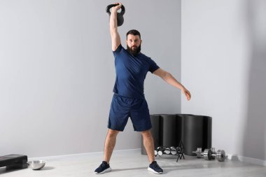 Spor salonunda kettlebell ile egzersiz yapan güçlü bir adam.