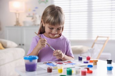 Beyaz masa içinde fırça çizen küçük kız.