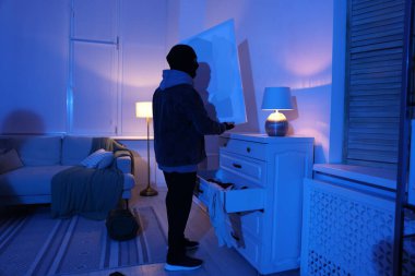 Yabancı evde maskeli bir hırsız resim çalıyor.