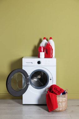 Modern çamaşır makinesi, deterjan ve zeytin duvarının yanındaki kıyafetler.