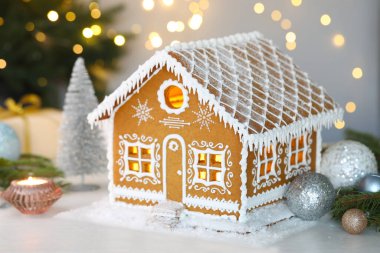 Güzel zencefilli kurabiye evi ve beyaz masanın üzerindeki Noel dekoru bulanık ışıklara karşı, yakın plan. Bokeh etkisi