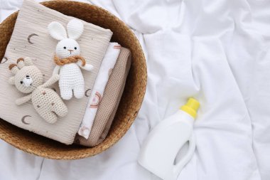 Çamaşır sepetinde katlanmış giysiler, oyuncaklar ve çarşafların üzerinde bir şişe deterjan.