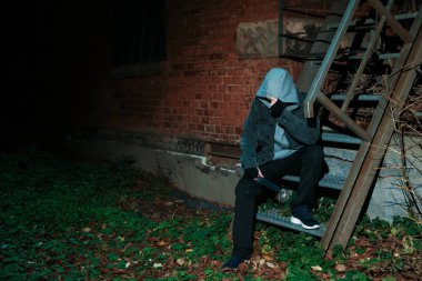 Kapüşonlu silahlı suçlu dışarıda tuğla binanın yanında, mesaj için yer var.