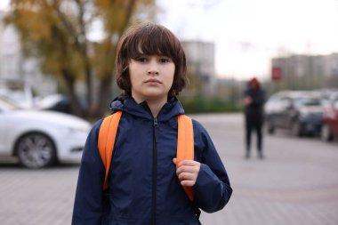 Sırt çantalı küçük bir çocuk dışarıda yürürken yabancı onu takip ediyor, seçici bir şekilde odaklanıyor. Çocuk tehlikede.