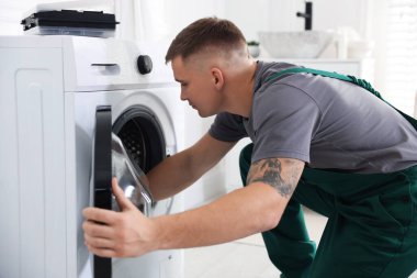 Tamirci evde bozuk çamaşır makinesini inceliyor.