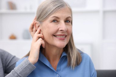 Evde annesinin kulağına işitme cihazı takan bir kadın var.