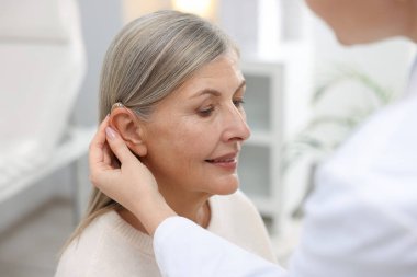 Doktor klinikte hastanın kulağına işitme cihazı takıyor.