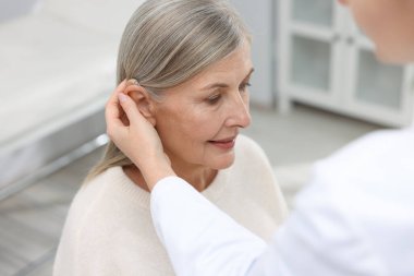 Doktor klinikte hastanın kulağına işitme cihazı takıyor.