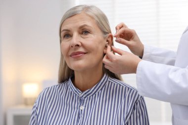 Doktor klinikte hastanın kulağına işitme cihazı takıyor.