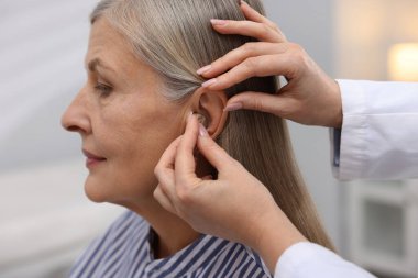 Doktor klinikte hastanın kulağına işitme cihazı takıyor.