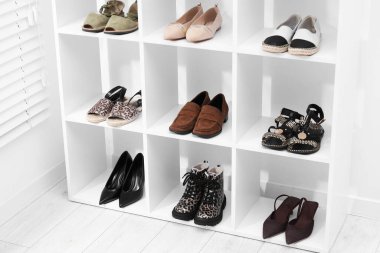 Beyaz duvarın yanındaki raflarda farklı ayakkabılar var.