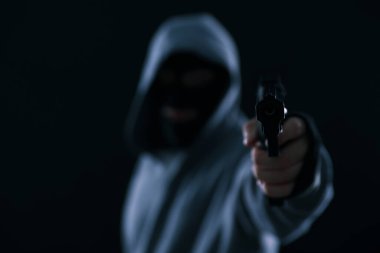 Siyah arka planda silahı olan maskeli bir suçlu, seçici odaklı. Metin için boşluk