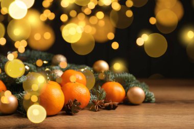 Taze mandalinalar, köknar dalları ve ahşap masa üzerindeki Noel süsleri, bokeh ışıkları.