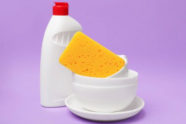 Mutfak süngeri, bulaşık deterjanı ve bulaşık takımı menekşe arka planda, yakın plan.
