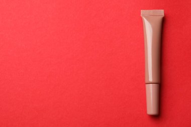 Beautiful nude lip gloss on red background, top view. Space for text
