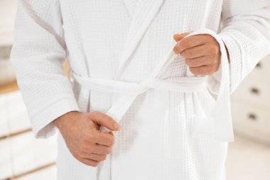 Bornozun kemerini bağlayan adam içeride, yakın plan.