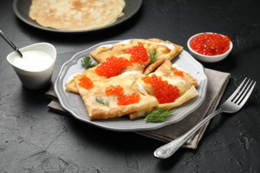 Kırmızı havyarlı leziz krepler ve siyah desenli masaya ekşi krema, yakın plan.