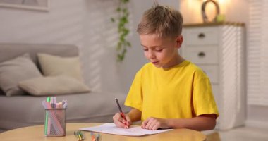 İçerideki ahşap masada resim çizen sevimli küçük çocuk.