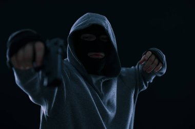 Siyah arka planda silahlı, maskeli bir suçlu.