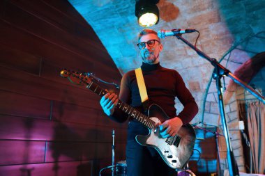 Sahnede elektro gitar çalan yakışıklı adam, düşük açılı görünüm.