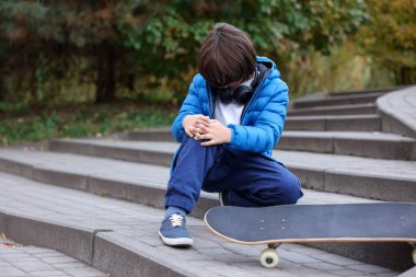 Dışarıda kaykay yaparken merdivenlerde diz ağrısı çeken küçük bir çocuk. Çocuk tehlikede.