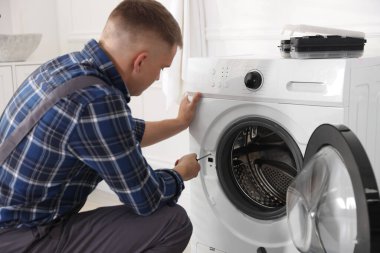 Üniformalı tamirci evde tornavidayla bozuk çamaşır makinesini tamir ediyor.