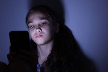 Siber tehlike. Karanlık arka planda telefon kullanan korkmuş bir kız.